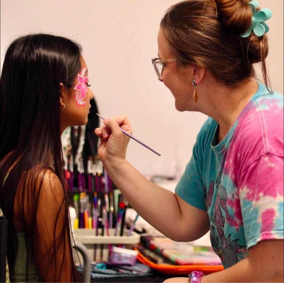 Tiah painting a pink hibiscus flower over a client's eye