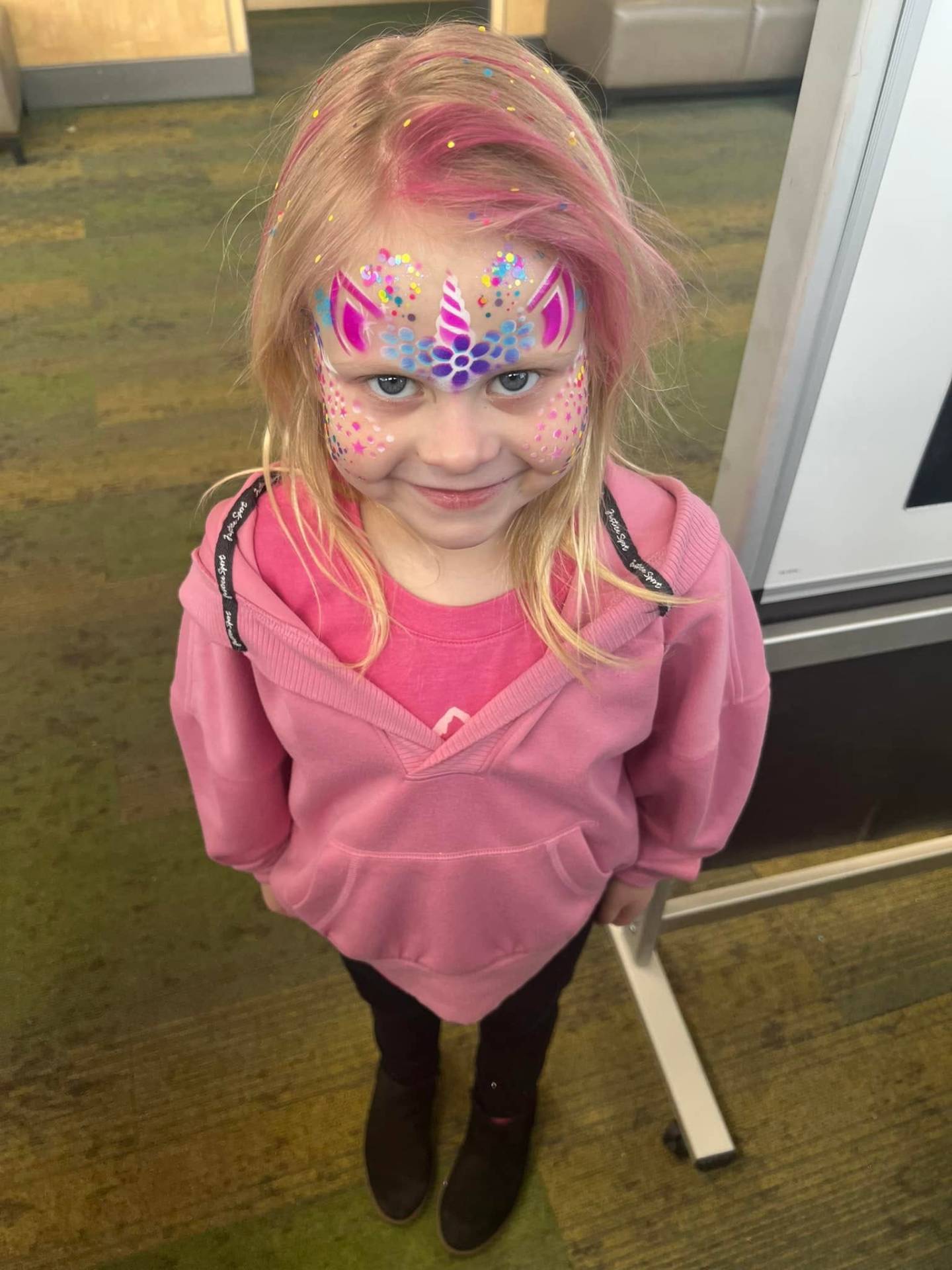 Pink and purple unicorn face paint with glitter on a young girl